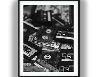 May include: A black and white framed wall art print featuring a collection of stacked vintage audio cassette tapes. The composition shows various plastic tape housings with visible spools, labels, and text including the brand name Maxell.