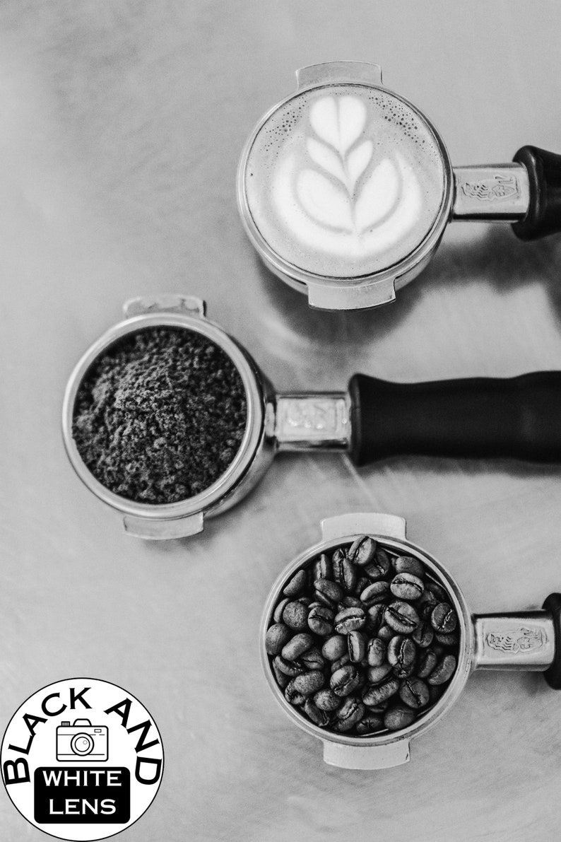 K&ouml;nnte beinhalten: Drei Espressoportafilter aus Metall, einer gef&uuml;llt mit Kaffeepulver, einer mit ganzen Kaffeebohnen und einer mit einem Latte-Art-Design.