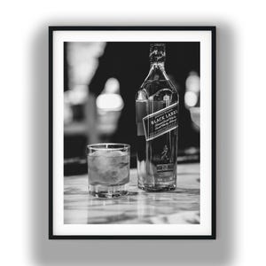 May include: A black and white photograph featuring a glass bottle of Johnnie Walker Black Label Scotch Whisky next to a short glass filled with ice cubes. The bottle label clearly displays the brand name and the number 12 in a square box.