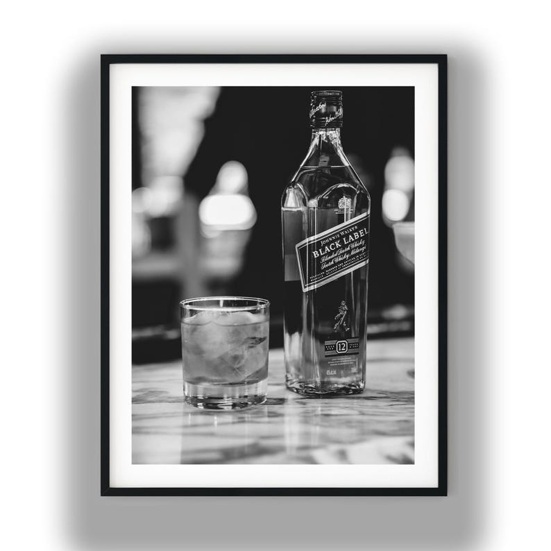May include: A black and white photograph featuring a glass bottle of Johnnie Walker Black Label Scotch Whisky next to a short glass filled with ice cubes. The bottle label clearly displays the brand name and the number 12 in a square box.