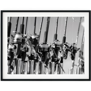May include: A black and white photo of multiple fishing rods with reels, all lined up in a row. The rods are all in focus, and the reels are all in focus. The background is blurred.