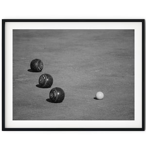 Puede incluir: Cuatro bolas de bolos negras y blancas están alineadas en un césped verde, con una bola de bolos blanca en primer plano.