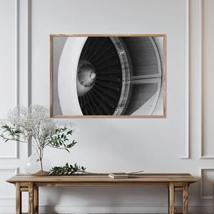 Puede incluir: Una impresión de arte mural en blanco y negro que presenta una vista de cerca de una turbina de motor a reacción con numerosas palas y un cono central, enmarcada en un marco de madera clara, mostrando detalles mecánicos.