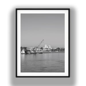 Barka rzeczna z dźwigiem, czarno-biała fotografia, grafika ścienna w stylu industrialnym do pobrania w wersji cyfrowej, wystrój marynistyczny, wydruk z panoramą miasta i rzeką