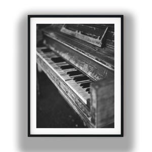 Peut inclure: Une impression d'art mural encadrée en noir et blanc présentant une vue en plongée d'un piano droit. L'image capture le clavier et le boîtier en bois de l'instrument avec une faible profondeur de champ, soulignant la texture des touches.