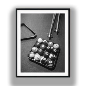 Puede incluir: Una impresión enmarcada en blanco y negro que muestra un estante cuadrado lleno de bolas de billar numeradas, dos tacos de billar con cabezales de puente cerca y un marco triangular sobre una superficie texturizada, capturando un juego.