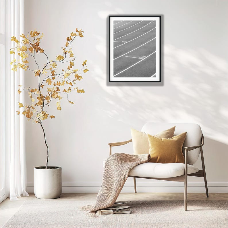 May include: A black and white framed wall art print featuring a high-angle view of a running track with white lane markings. The artwork is displayed in a thin black frame, showcasing the geometric lines and curves of the athletic track surface.