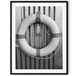 Puede incluir: Una fotografía en blanco y negro de un salvavidas blanco colgado de una pared de metal corrugado.