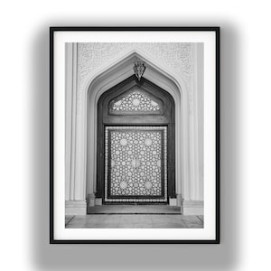 May include: A black and white framed print featuring an arched doorway with intricate geometric patterns. The door is set within a stone frame with detailed carvings and a hanging lantern, presented in a clean, minimalist black frame.