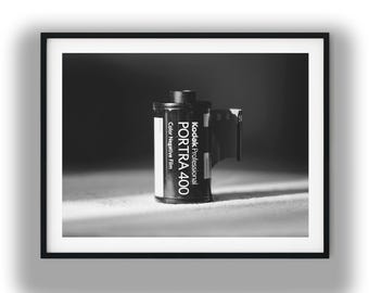 May include: Black and white framed photograph of a Kodak Professional Portra 400 color negative film canister. The film canister is black with white text and a white label. The photograph is in a black frame.