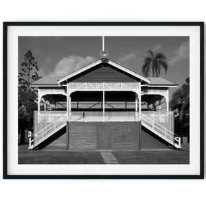 May include: A black and white photograph of a wooden pavilion with a white roof and white railings. The pavilion has two sets of stairs leading up to it. The pavilion is surrounded by grass and trees.