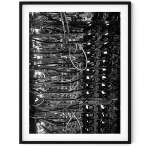 Puede incluir: Una foto en blanco y negro de un rack de servidor con muchos cables y alambres conectados a él.