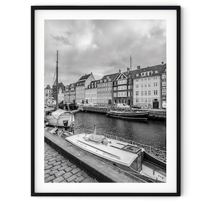 Pode incluir: Fotografia a preto e branco de um canal em Copenhaga, Dinamarca. O canal é ladeado por edifícios coloridos e barcos estão atracados ao longo da margem.