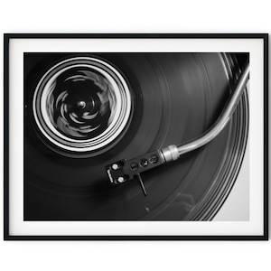May include: A black and white photo of a record player with a vinyl record spinning on the turntable. The needle is in the groove of the record and the tonearm is extended. The record is spinning and the label is visible in the center.