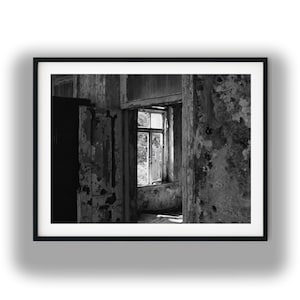 May include: Black and white framed print of an interior space with a window. The walls and door frames show peeling paint, suggesting age and decay. The window offers a view of the outside, with light streaming in.