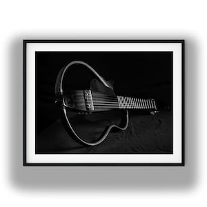 May include: A black and white photograph of a silent guitar with a hollow, circular frame design. The instrument features a long neck with frets, a bridge, and strings, presented in a minimalist, skeletal structure against a dark background.