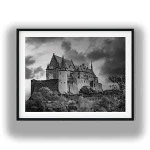 Può includere: Stampa incorniciata in bianco e nero di un castello medievale. Il castello, con le sue torri e la sua complessa architettura, è arroccato su una collina sotto un cielo drammatico e nuvoloso. La stampa è in una cornice nera.