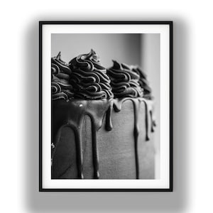 Può includere: Una fotografia in bianco e nero di una torta caratterizzata da una superficie glassata liscia con spesse colature di ganache al cioccolato che scendono lungo i lati, sormontata da diversi ciuffi di glassa disposti lungo il bordo superiore.
