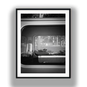 May include: Black and white framed photograph of a vehicle's window, offering a view of a park with trees and benches. The interior of the vehicle is visible, with a glimpse of a seat and other details.