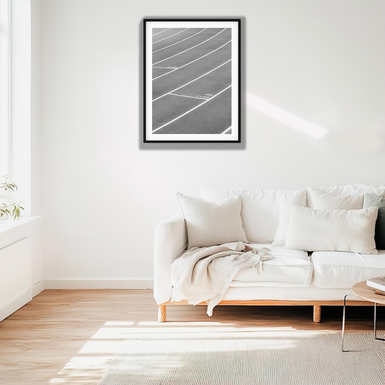 May include: A black and white framed wall art print featuring a high-angle view of a running track with white lane markings. The image shows the curved lines of the track surface extending across the frame, captured in a monochromatic style.