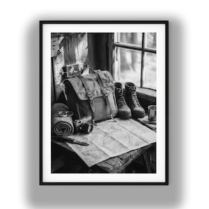 May include: Black and white photograph of a travel scene. A canvas backpack, hiking boots, a rolled blanket, a camera, a compass, a map, a knife, and a metal cup are arranged on a wooden surface near a window.