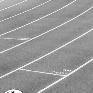May include: A black and white photograph of a running track with multiple lanes marked by white lines. The surface is textured, and white text markings indicate 4x400, 4x100, and 400 distances. A circular logo with a camera icon and text reads BLACK AND WHITE LENS.