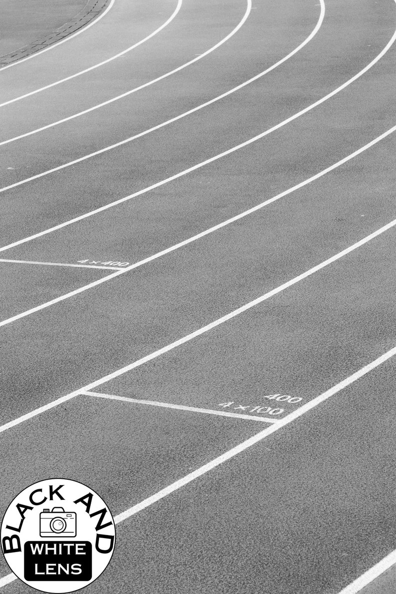 May include: A black and white photograph of a running track with multiple lanes marked by white lines. The surface is textured, and white text markings indicate 4x400, 4x100, and 400 distances. A circular logo with a camera icon and text reads BLACK AND WHITE LENS.