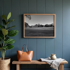 Könnte beinhalten: Ein gerahmtes Schwarz-Weiß-Foto eines Sportplatzes hängt an einer tealblauen Wand. Eine braune Ledertasche liegt auf einer Holzbank unter dem Foto. Eine Topfpflanze und ein kleiner Keramikkrug befinden sich ebenfalls auf der Bank.