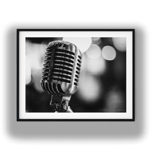 May include: A black and white photograph of a vintage-style dynamic microphone with a metallic, ribbed grille. The microphone is mounted on a swivel stand, captured in sharp focus against a soft, out-of-focus background with circular light bokeh.