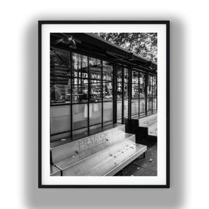 May include: A black and white photograph of a storefront with large glass windows and a metal frame. In front of the building, there are tiered metal steps featuring faint graffiti markings. The scene is captured in a high-contrast monochrome style.