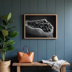 May include: Black and white framed print of a burlap sack overflowing with coffee beans. The print hangs on a blue wall above a wooden bench. A brown leather tote bag and a plant in a woven basket are also visible.