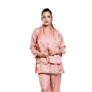May include: A woman wearing a blush pink pantsuit with a long-sleeved top and matching trousers. The pantsuit has a subtle striped pattern and the woman is wearing nude heels.