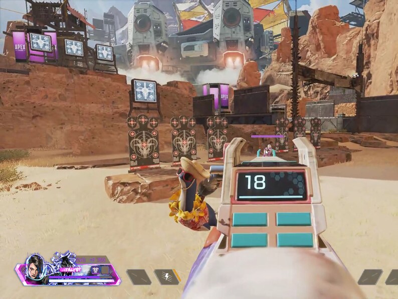 Op de afbeelding: Een videogamescherm dat een first-person perspectief laat zien van een speler die met een wapen op een schietbaan mikt. De speler gebruikt een roze en wit wapen met een digitaal display dat het nummer 18 laat zien. De schietbaan bevindt zich in een woestijnomgeving met een grote metalen structuur op de achtergrond.