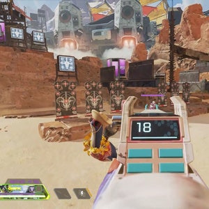 May include: A first-person perspective from a video game. The player's weapon is in view, showing the number 18 on a digital display. The background features a desert environment with structures and targets. The game's interface is at the bottom.