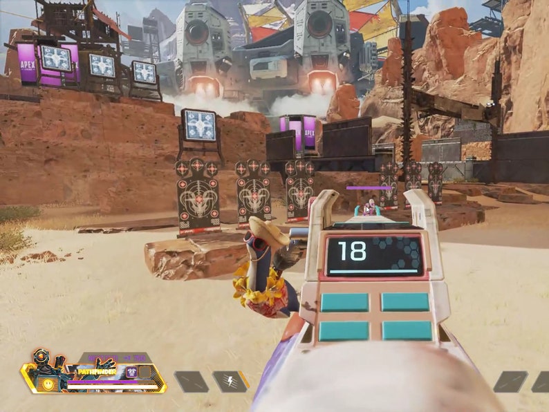 Op de afbeelding: Eerste-persoonsweergave van een videogame-sc&egrave;ne. Het wapen van de speler staat centraal en toont het digitale nummer 18. De achtergrond toont een woestijnlandschap met structuren en doelen. De spelinterface is zichtbaar.