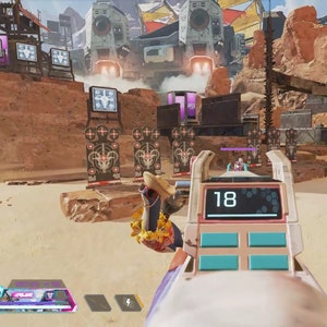 May include: A pink and white shooting range target with a digital display showing the number 18. The target is in a desert-like environment with a large metal structure in the background.