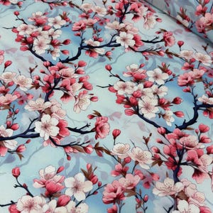 May include: A fabric with a repeating floral pattern of pink and white cherry blossoms on dark brown branches against a light blue background. The blossoms are in full bloom, with some buds visible.
