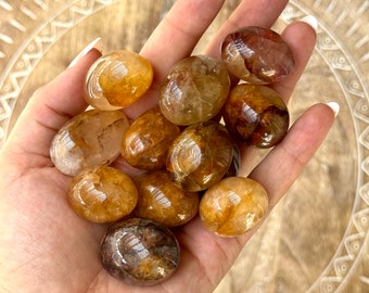 May include: A collection of tumbled citrine stones in various shades of yellow and brown. The stones are smooth and polished, with a translucent appearance.