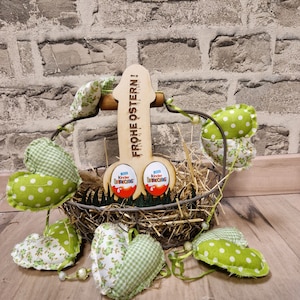 Könnte beinhalten: Eine hölzerne Osterdekoration mit dem Text "Frohe Ostern!" Die Dekoration ist in Form eines Hasen und hält einen Korb mit grünen und weißen gepunkteten Herzen und zwei Schokoladeneiern.