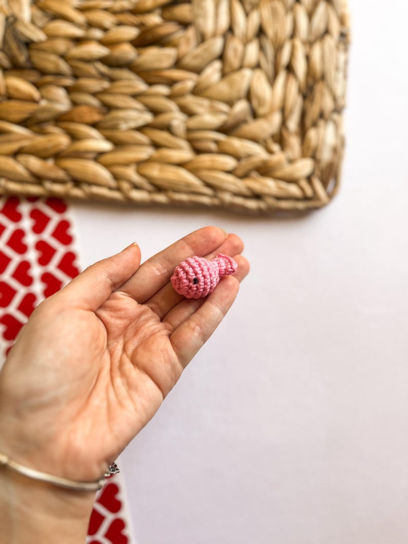 Puede incluir: Un peque&ntilde;o adorno de coraz&oacute;n de color rosa tejido a crochet. El adorno se sostiene en la mano de una persona.