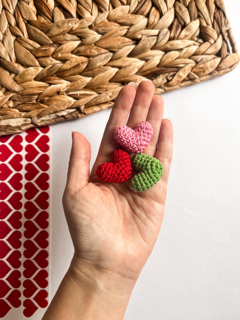 May include: Three small crocheted hearts in pink, red, and green. The hearts are held in a hand.