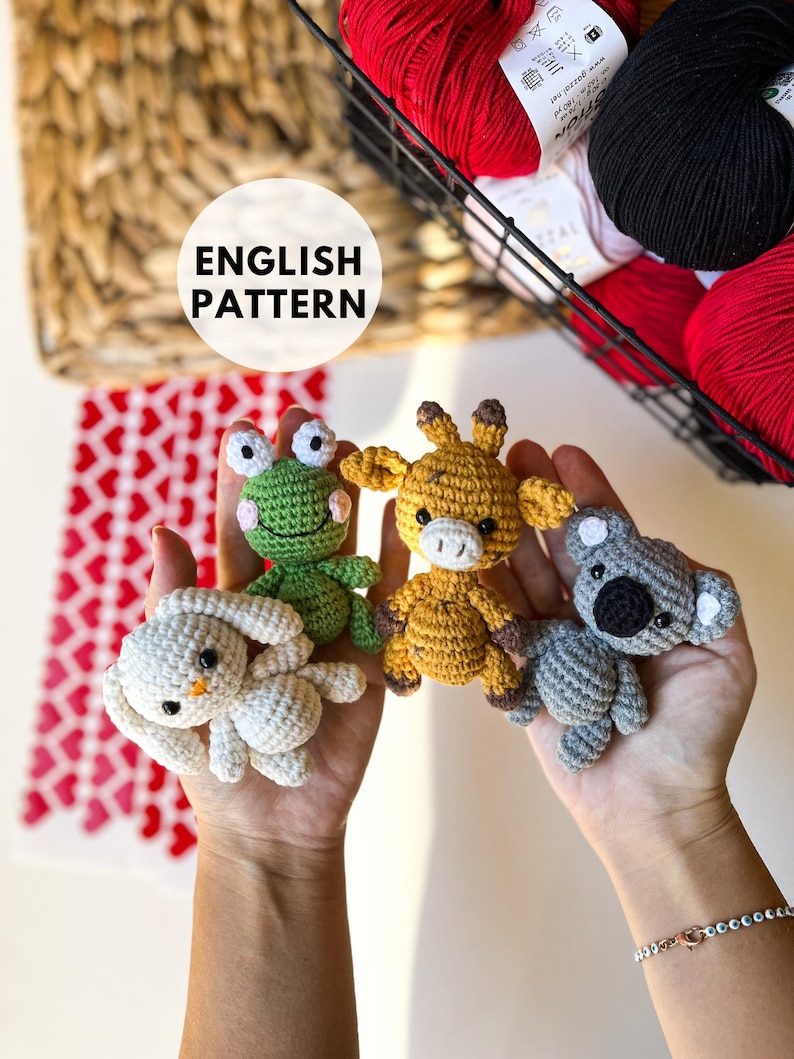 Puede incluir: Cuatro animales de amigurumi de crochet: una rana verde, una jirafa amarilla, un conejito blanco y un koala gris. Los animales est&aacute;n sostenidos en las manos de una persona. La imagen incluye el texto "ENGLISH PATTERN".