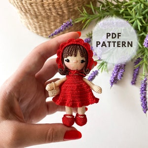 May include: Crochet amigurumi doll pattern, PDF download. The doll is wearing a red dress and a red hooded cape with white trim. The doll has brown hair and brown eyes.