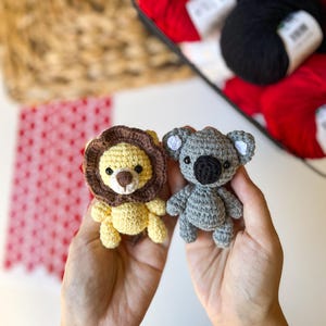 Puede incluir: Dos animales de peluche tejidos a crochet, un le&oacute;n amarillo y un koala gris, se sostienen en las manos de una persona. El le&oacute;n tiene una melena marr&oacute;n y ojos negros. El koala tiene ojos negros y una nariz negra.