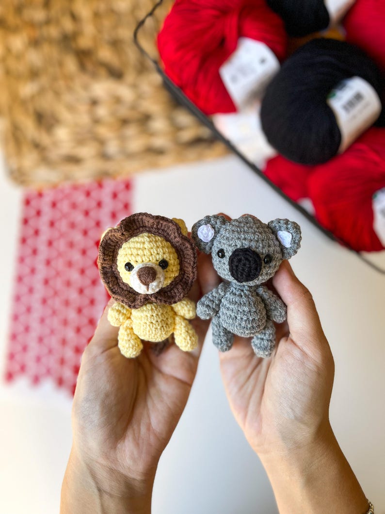 Puede incluir: Dos animales de peluche tejidos a crochet, un le&oacute;n amarillo y un koala gris, se sostienen en las manos de una persona. El le&oacute;n tiene una melena marr&oacute;n y ojos negros. El koala tiene ojos negros y una nariz negra.