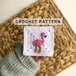 May include: Crochet pattern for a flamingo square. The square is white with a pink flamingo in the center. The flamingo has a black eye and brown legs.
