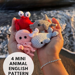 Puede incluir: Cuatro juguetes de animales en miniatura de crochet: un cangrejo rojo, un delfín gris, un pulpo rosa y una ballena azul. Los juguetes están en las manos de una persona. La imagen incluye el texto "4 Mini Animal English Pattern".