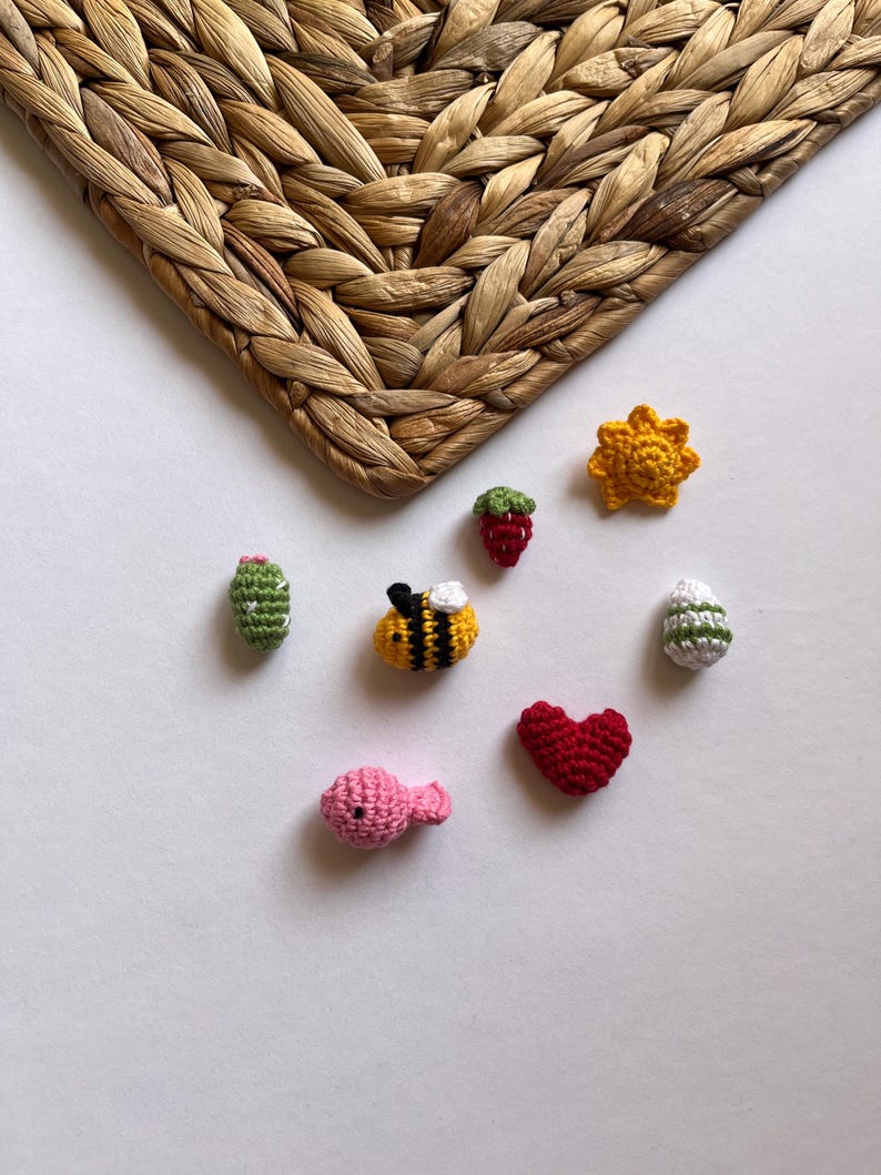 Puede incluir: Una colecci&oacute;n de peque&ntilde;os art&iacute;culos tejidos a crochet, que incluyen una abeille, un coraz&oacute;n, un pez, un cactus, una fresa, un sol y un huevo. Los art&iacute;culos est&aacute;n hechos con hilo de diferentes colores y est&aacute;n dispuestos sobre un fondo blanco.