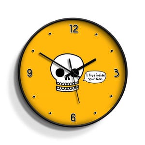 Puede incluir: Un reloj redondo amarillo con números y manecillas negros. La esfera del reloj presenta una calavera en blanco y negro con el texto "Vivo dentro de tu cara."