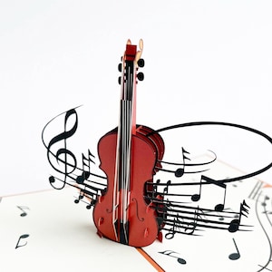 Könnte beinhalten: Eine rote Papier-Violine mit schwarzen Noten und Symbolen. Die 3D-Pop-up-Karte zeigt ein detailliertes Geigen-Design mit Saiten und einem Bogen, umgeben von Noten auf weißem Hintergrund.
